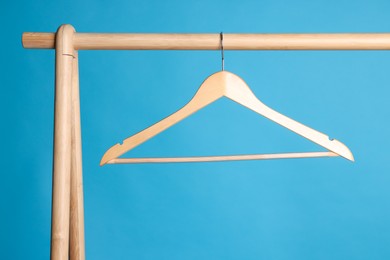Photo of Empty clothes hanger on wooden rack against light blue background