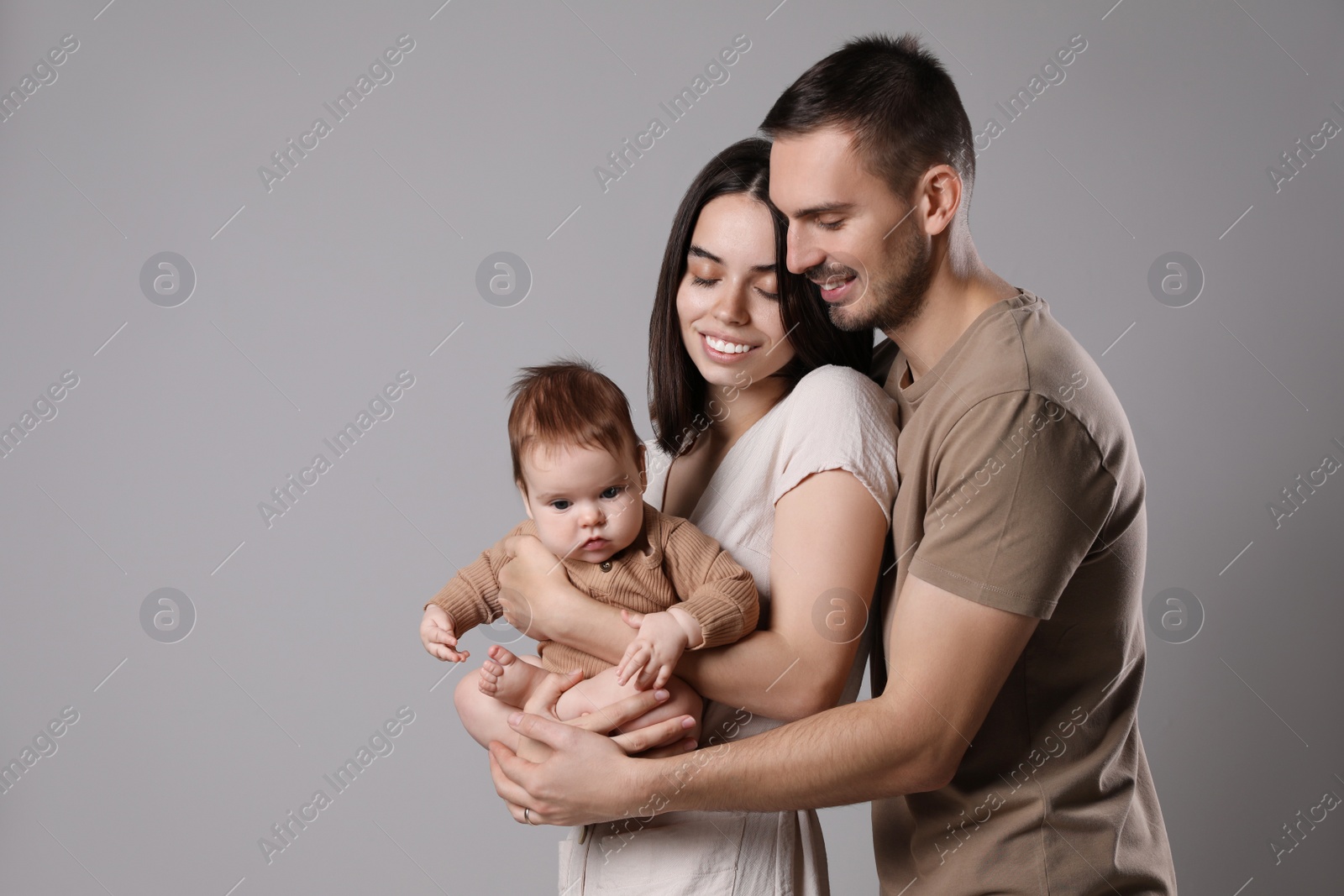 Photo of Happy family. Couple with their cute baby on grey background, space for text