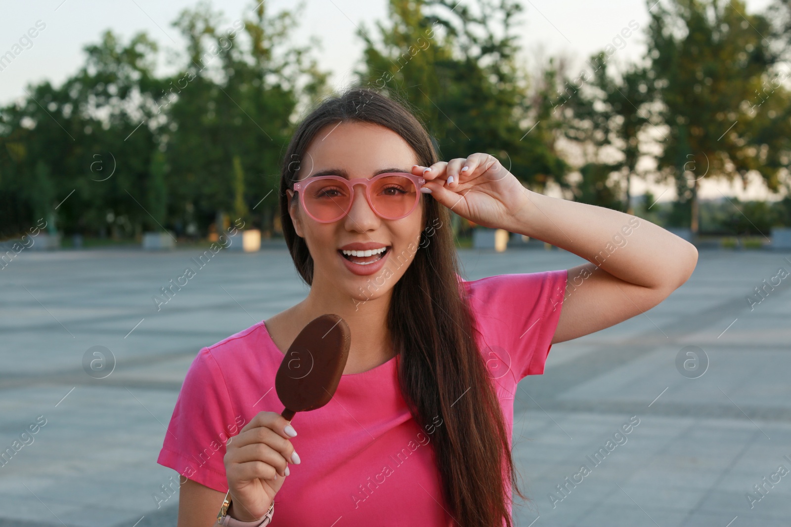 Photo of Beautiful young woman holding ice cream glazed in chocolate on city street