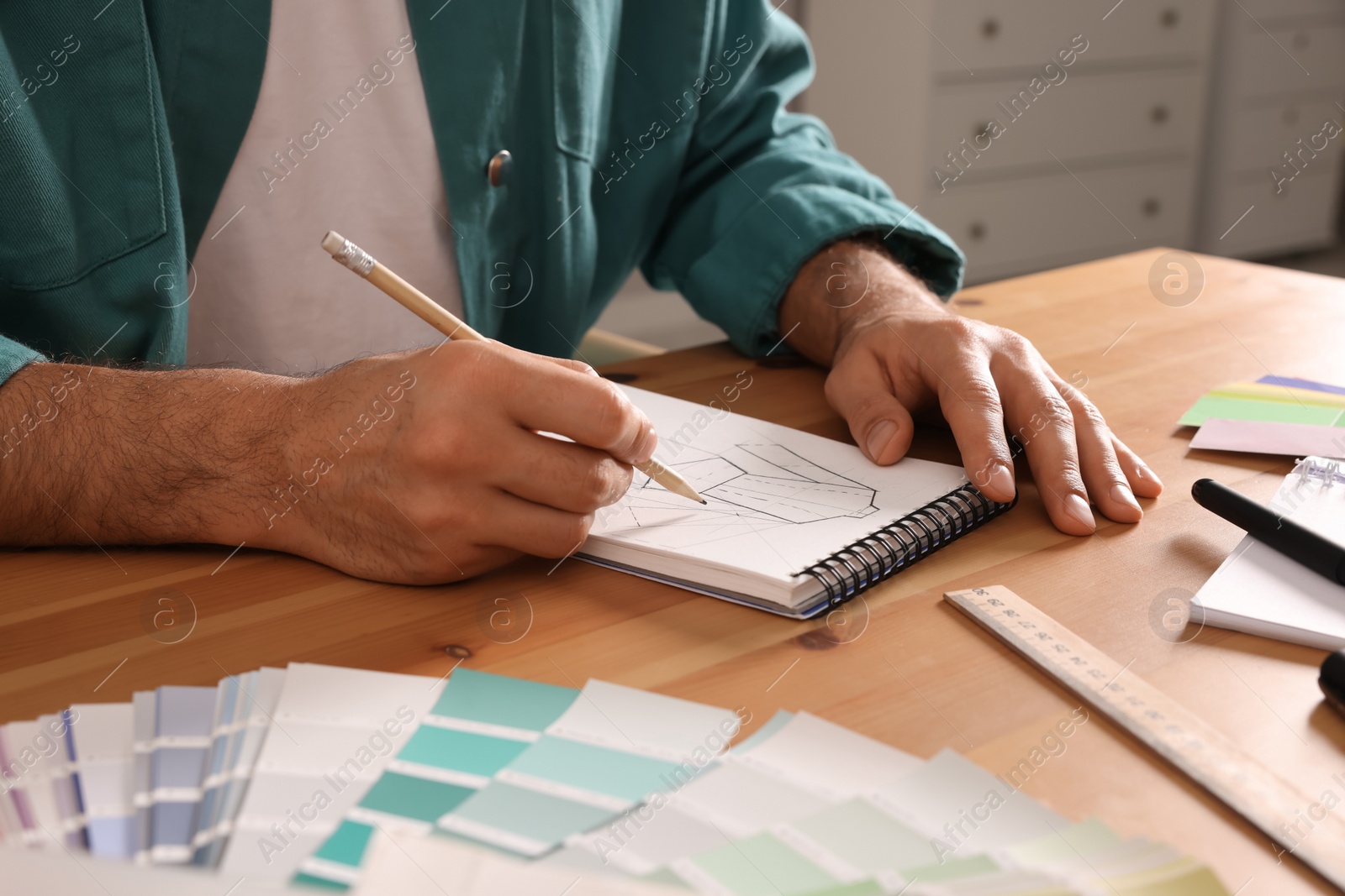 Photo of Man drawing in sketchbook with pencil at wooden table indoors, closeup