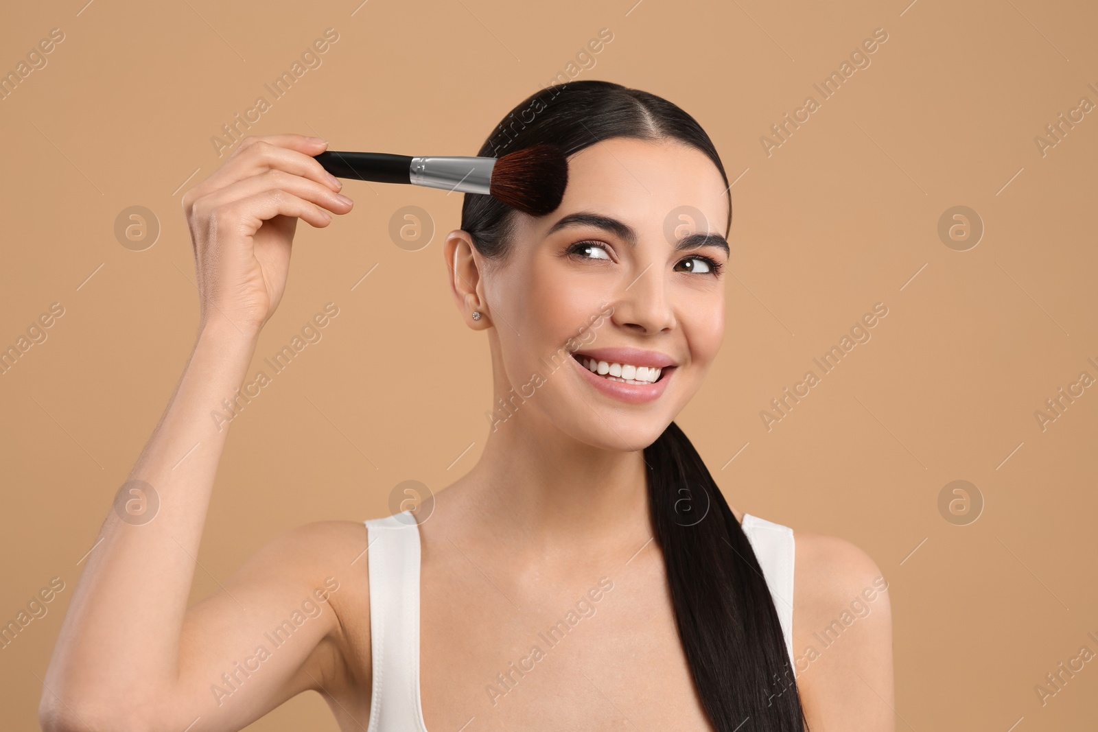 Photo of Beautiful woman applying makeup on light brown background