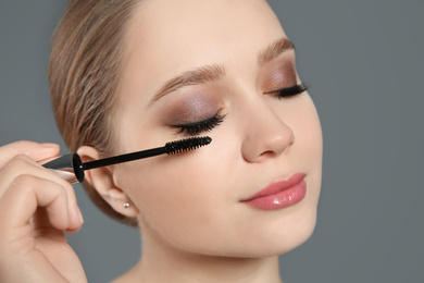 Photo of Beautiful woman applying mascara on light grey background. Stylish makeup