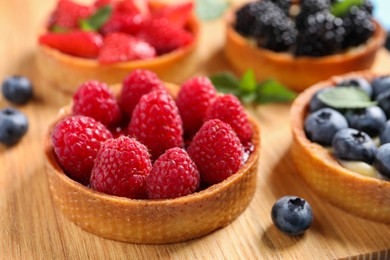 Photo of Tartlet with fresh raspberries on wooden board, closeup. Delicious dessert