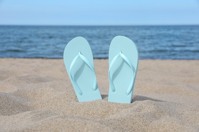 Stylish light blue flip flops on beach sand