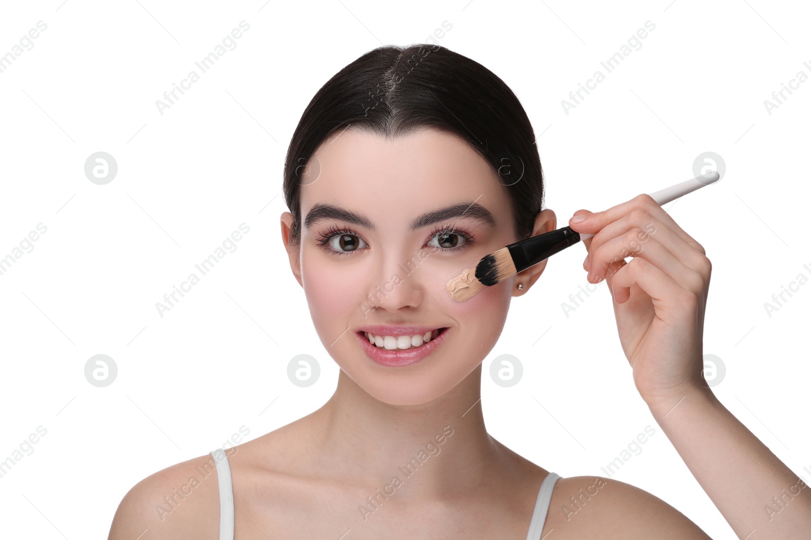 Photo of Teenage girl applying foundation on face with brush against white background