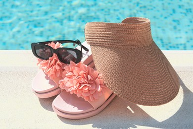 Photo of Stylish visor cap, slippers and sunglasses near outdoor swimming pool on sunny day