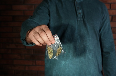 Photo of Male dealer holding hemp in plastic bag near brick wall, closeup