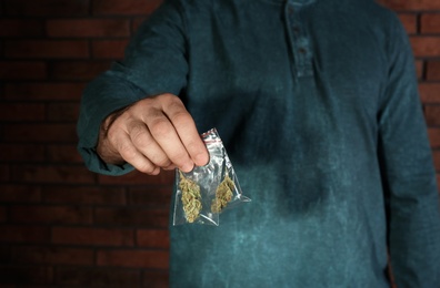 Male dealer holding hemp in plastic bag near brick wall, closeup