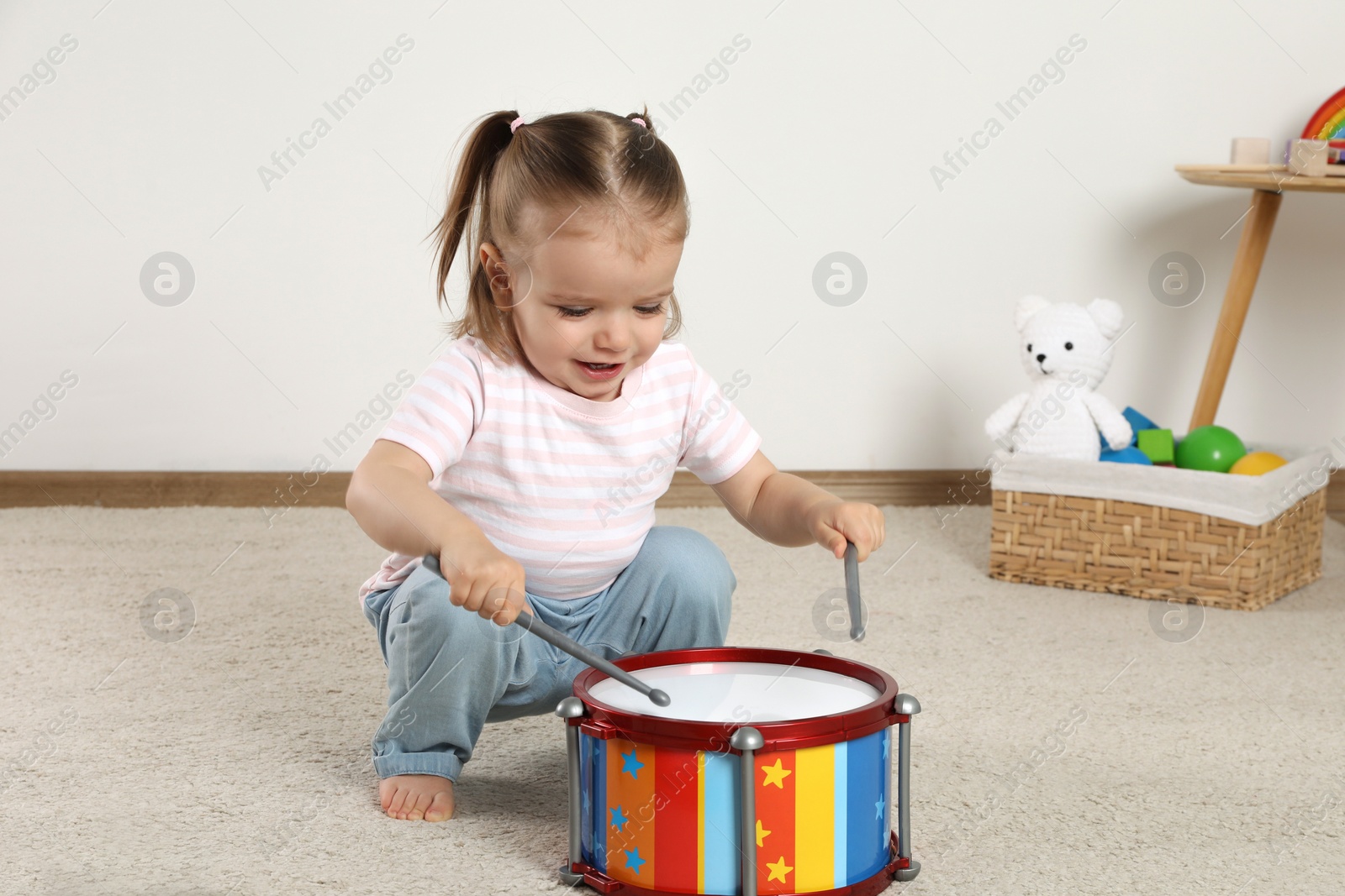 Photo of Cute little girl playing with drum and drumsticks at home