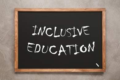 Image of Small blackboard with word INCLUSIVE EDUCATION on light grey stone background, top view