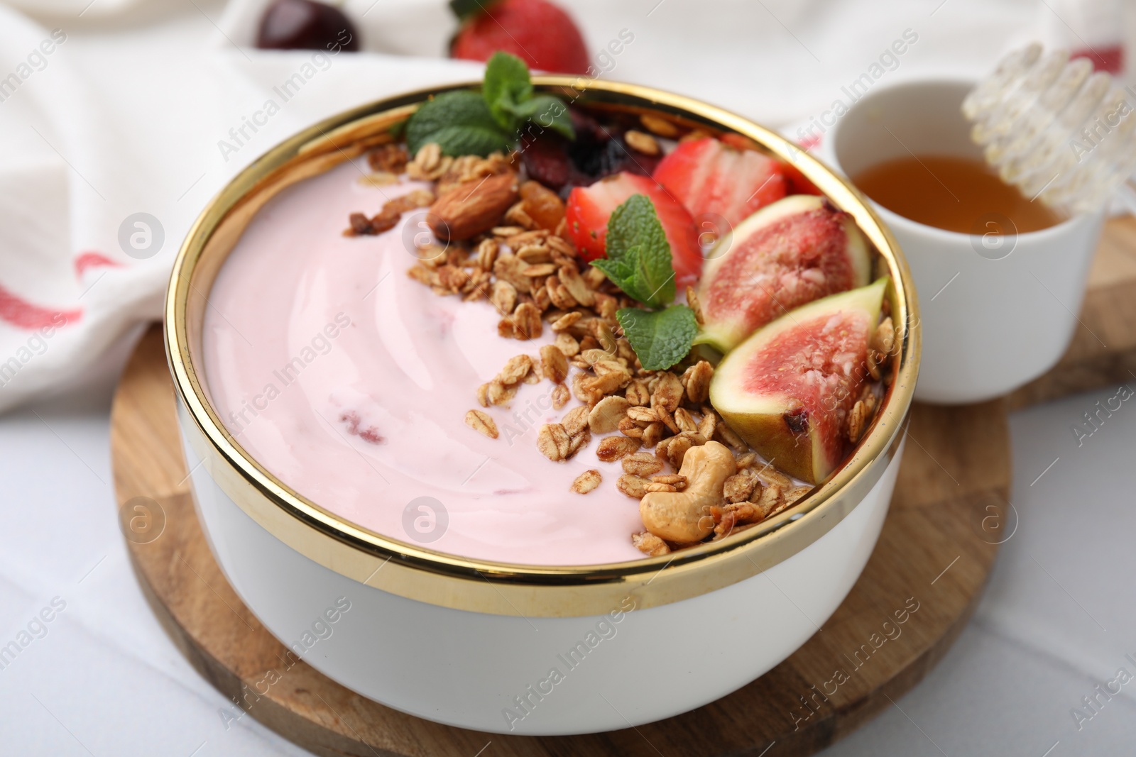 Photo of Bowl with yogurt, fruits and granola on white tiled table, closeup