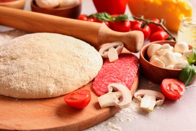 Photo of Pizza dough, products and rolling pin on gray table, closeup