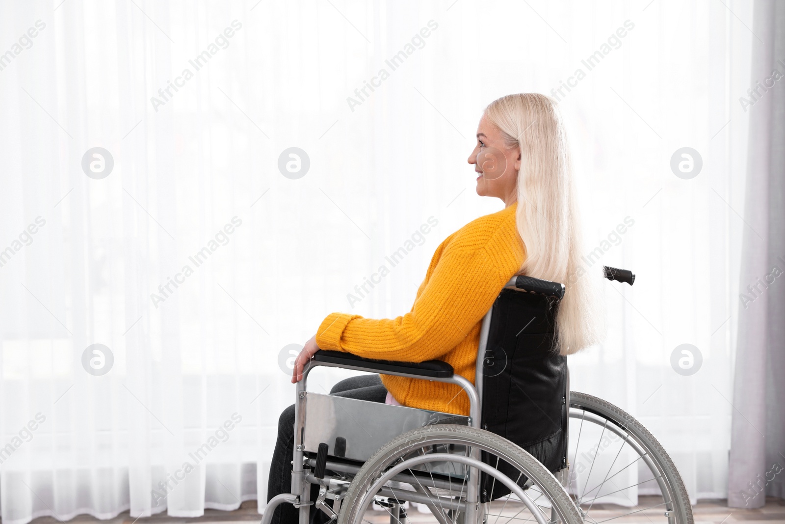 Photo of Mature woman sitting in wheelchair near window at home