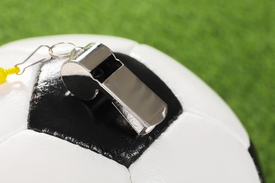 Photo of Football referee equipment. Soccer ball and metal whistle on green background, closeup