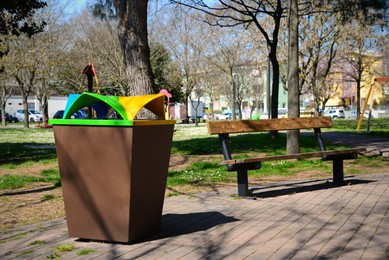 Trash bin and wooden bench in park on sunny day
