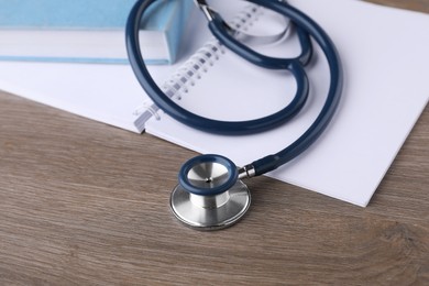 Photo of Book, stethoscope and notebook on wooden table, closeup. Medical education