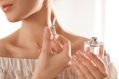 Young woman applying perfume on neck against blurred background, closeup
