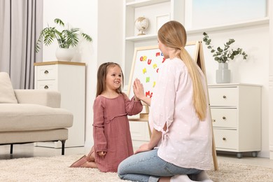 Photo of Mom and daughter giving each other high five while learning alphabet with magnetic letters at home