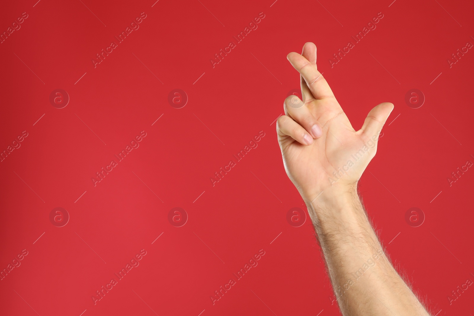 Photo of Man with crossed fingers and space for text on red background, closeup. Superstition concept