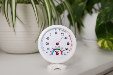 Photo of Round hygrometer with thermometer and plants on white table
