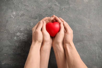 Photo of People holding red heart on gray background, top view. Cardiology concept