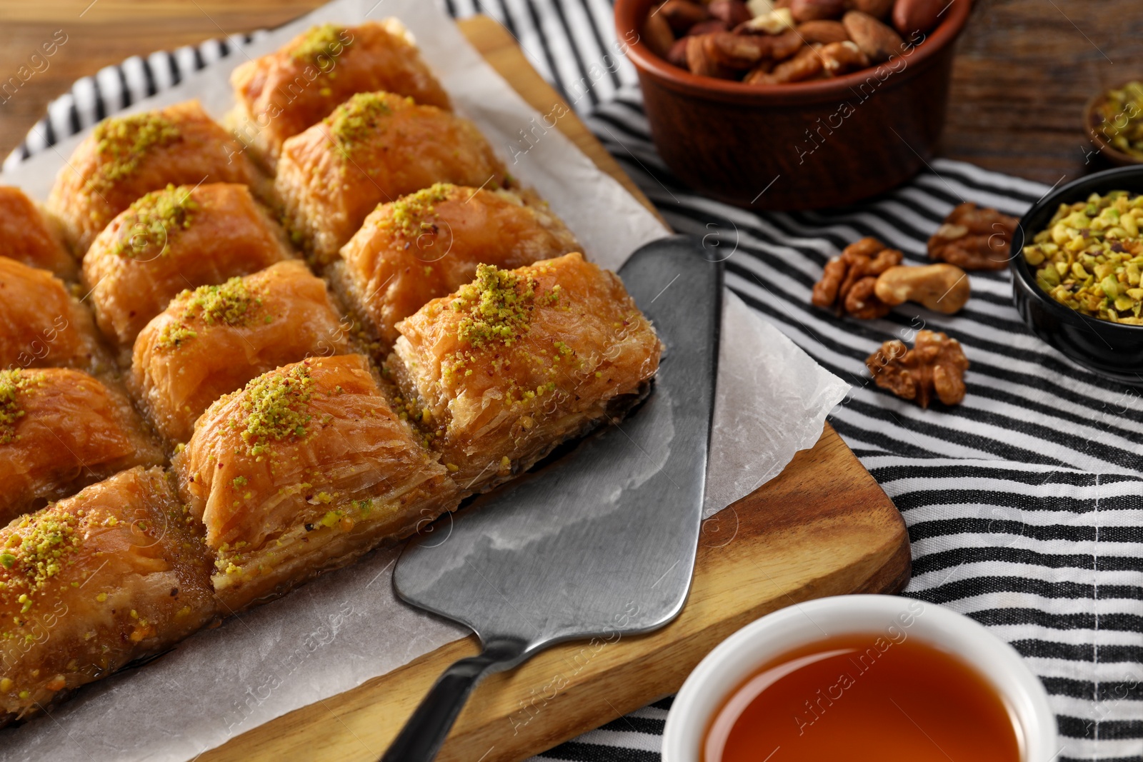 Photo of Delicious sweet baklava with pistachios and cake server on table, closeup