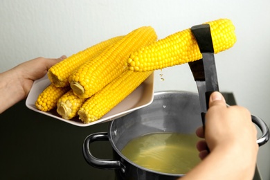 Photo of Young woman taking boiled corn cob from pot on stove, closeup