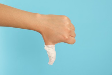 Woman showing thumb down wrapped in medical bandage on light blue background, closeup