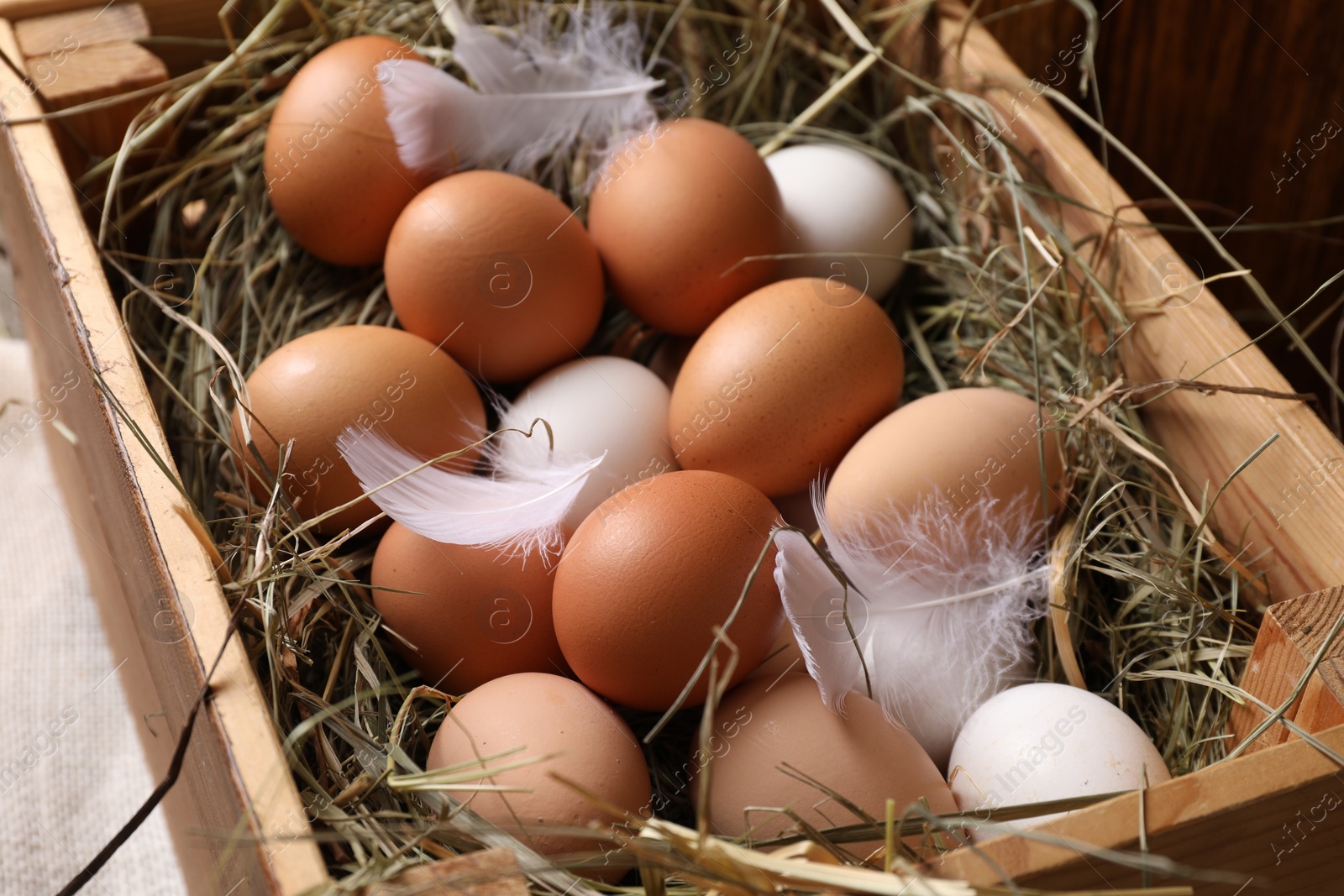 Photo of Fresh chicken eggs and dried hay in wooden crate on table, closeup