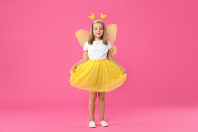 Photo of Cute little girl in fairy costume with yellow wings on pink background