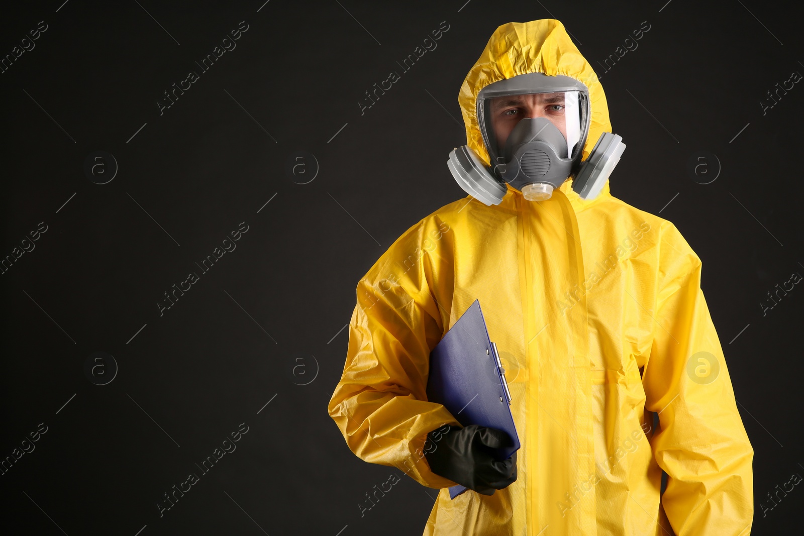 Photo of Man in chemical protective suit holding clipboard on black background, space for text. Virus research