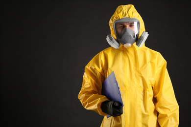 Man in chemical protective suit holding clipboard on black background, space for text. Virus research