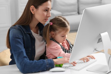 Photo of Woman working remotely at home. Mother and her daughter at desk with computer