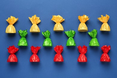 Photo of Many candies in colorful wrappers on blue background, flat lay