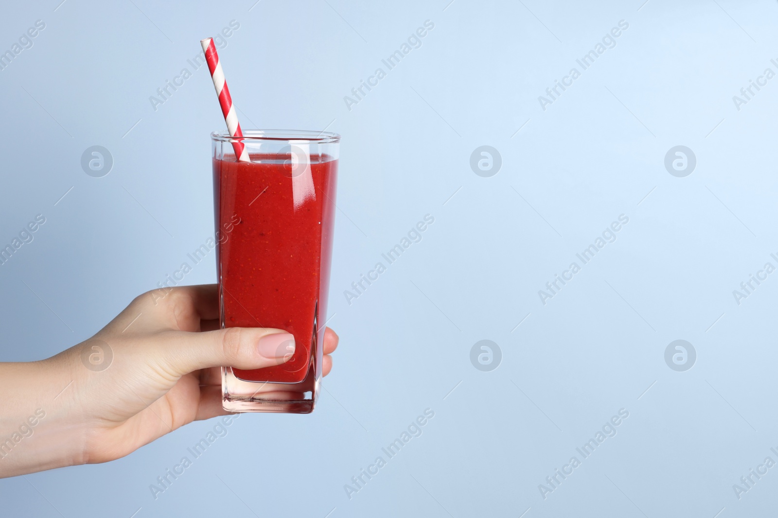 Photo of Woman holding glass of tasty smoothie on light blue background, closeup. Space for text