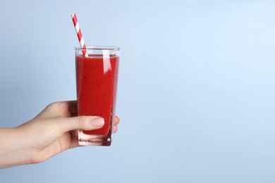 Photo of Woman holding glass of tasty smoothie on light blue background, closeup. Space for text