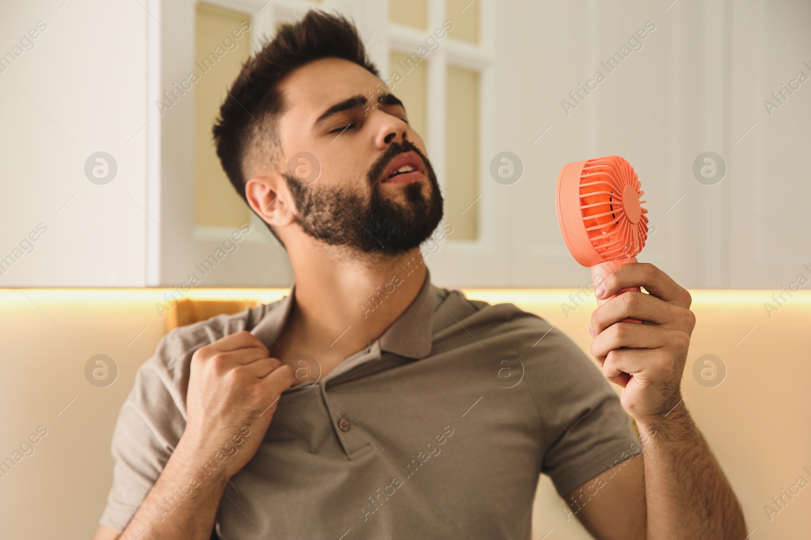 Photo of Man with portable fan suffering from heat at home. Summer season