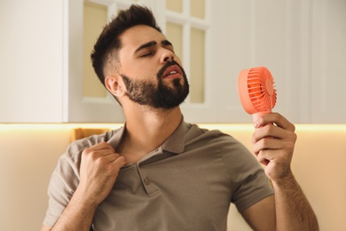 Man with portable fan suffering from heat at home. Summer season