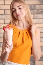 Photo of Young woman with glass of delicious milk shake on brick wall background