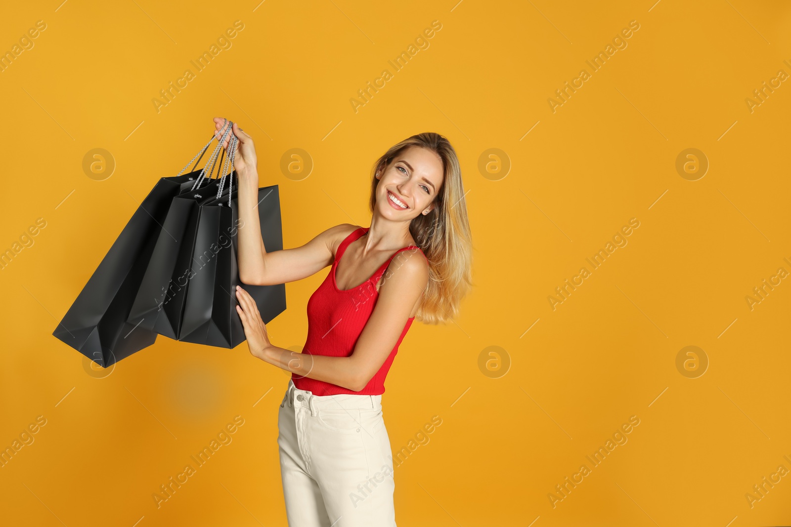 Photo of Happy young woman with shopping bags on yellow background. Black Friday Sale