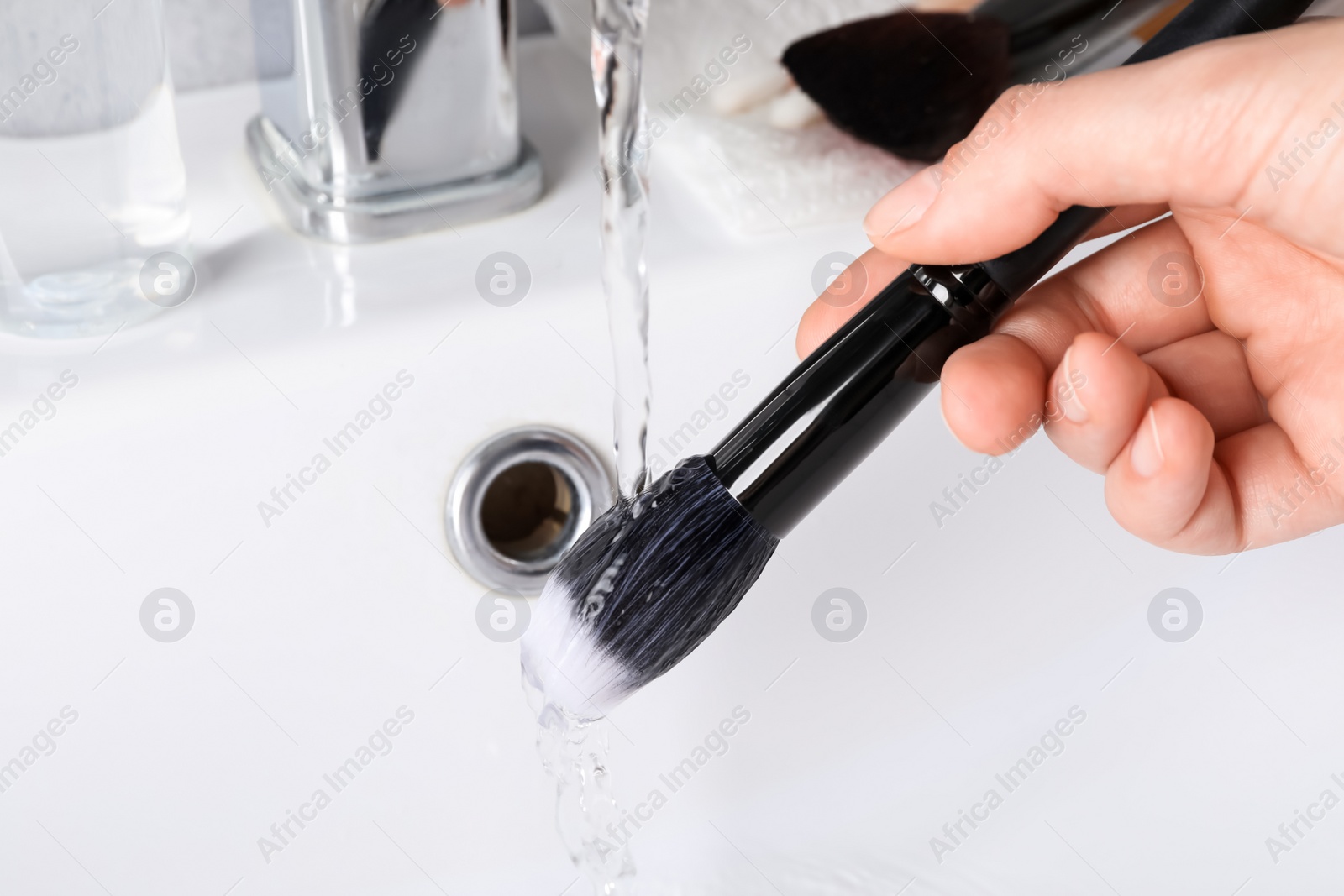 Photo of Woman washing makeup brush under stream of water in sink, closeup