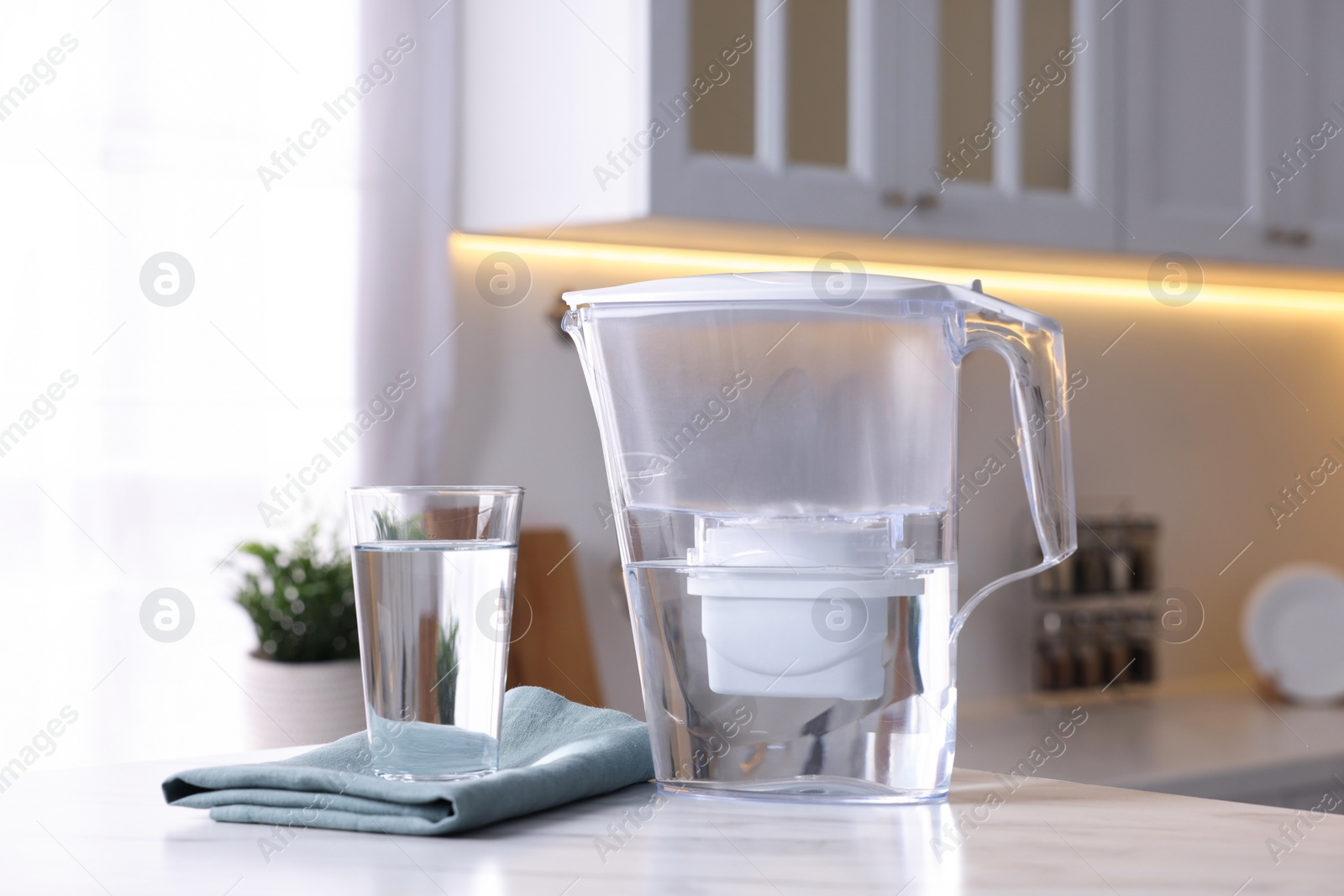 Photo of Water filter jug and glass on white marble table in kitchen, closeup