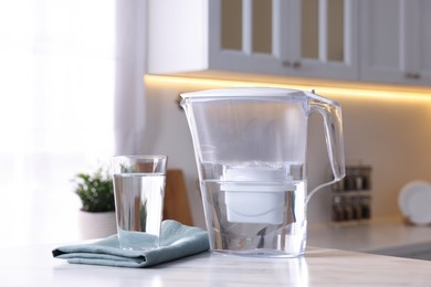 Photo of Water filter jug and glass on white marble table in kitchen, closeup