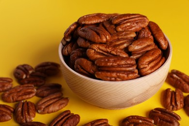 Tasty pecan nuts with bowl on yellow background, closeup