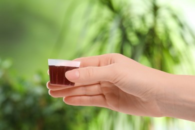 Woman holding measuring cup with syrup on blurred background, closeup. Cold medicine
