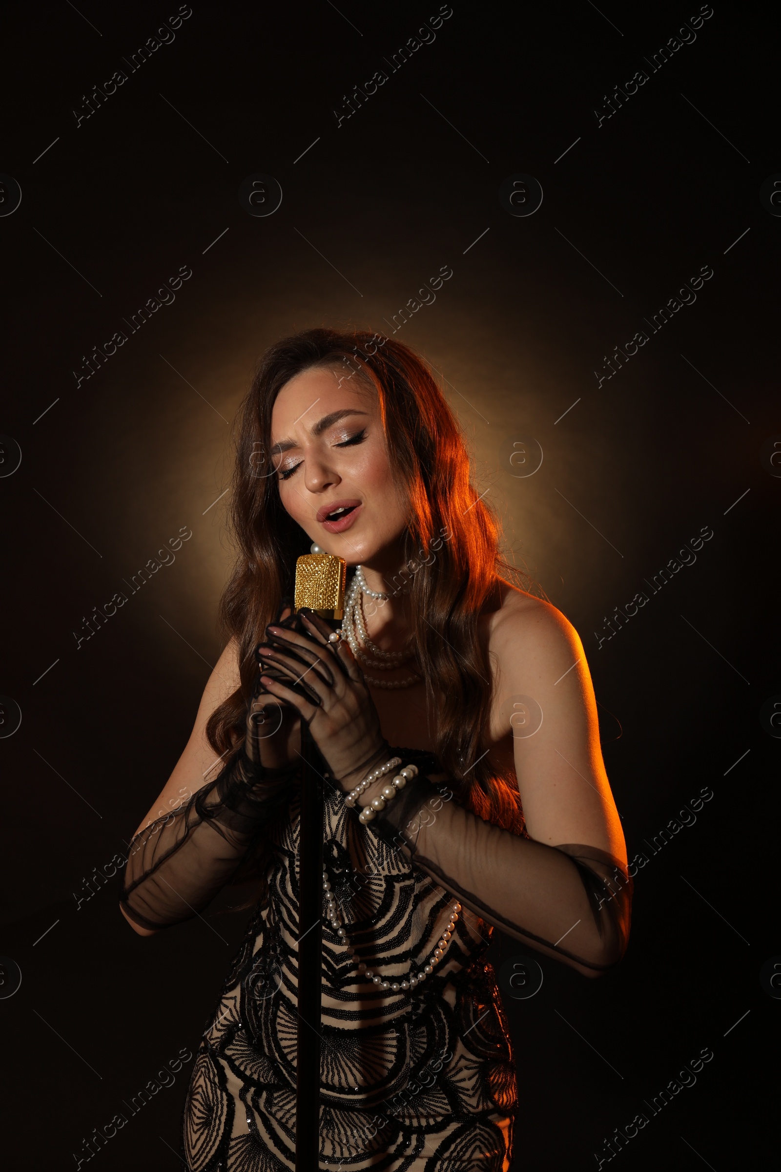 Photo of Beautiful young woman in stylish dress with microphone singing on dark background