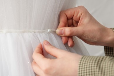 Photo of Dressmaker pinning pearl at mannequin with wedding dress in atelier, closeup
