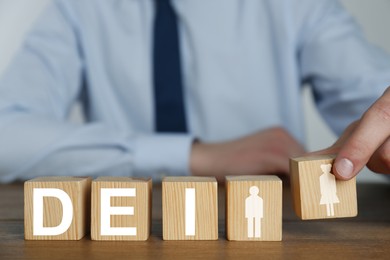 Image of Concept of DEI - Diversity, Equality, Inclusion. Businessman and wooden cubes with letters and image of people on table, closeup