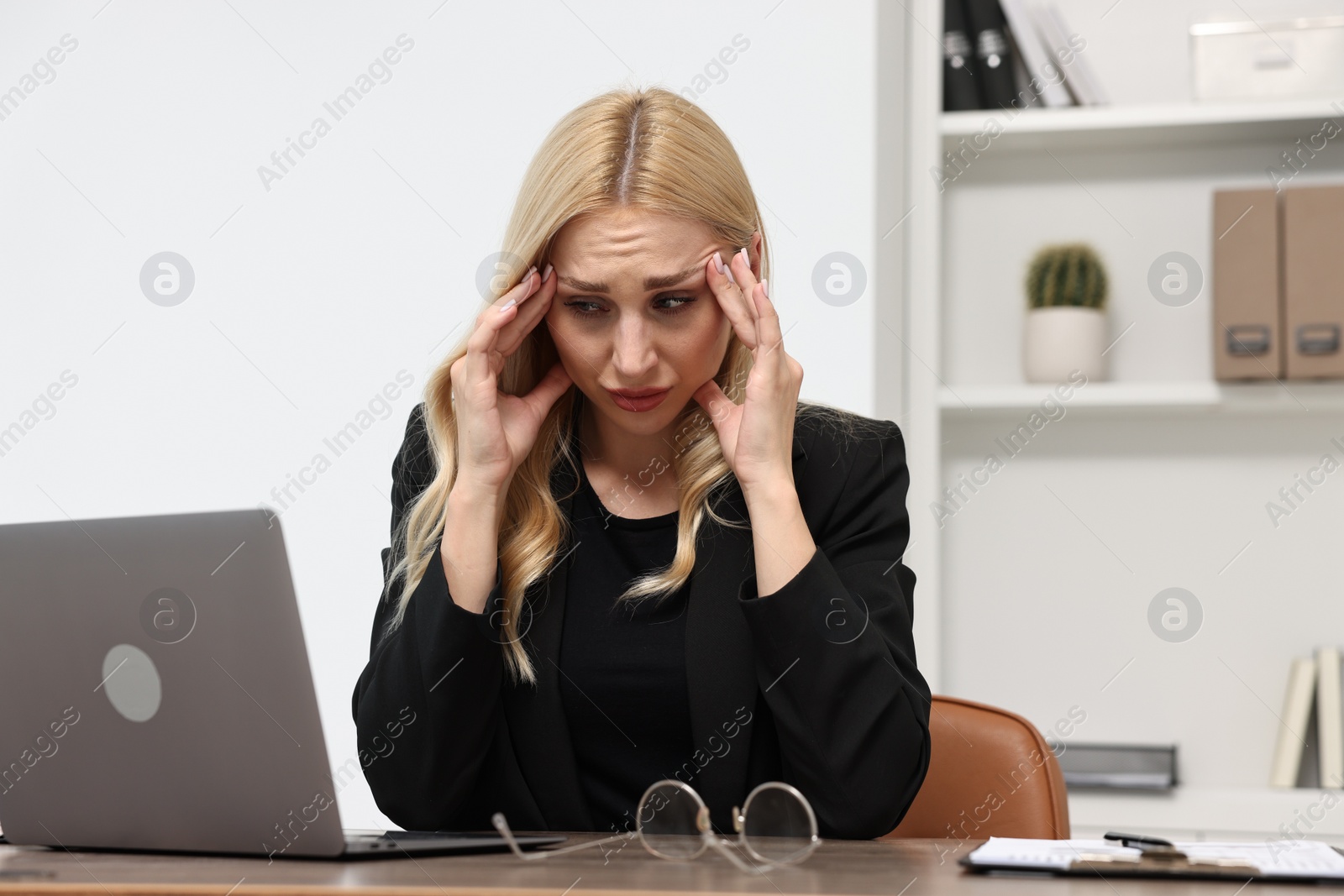 Photo of Overwhelmed woman at table with laptop and glasses in office