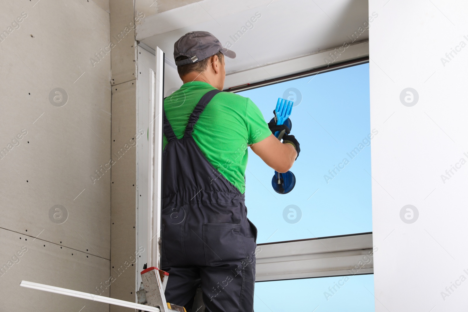 Photo of Worker using suction lifter for double glazing window installation indoors, back view